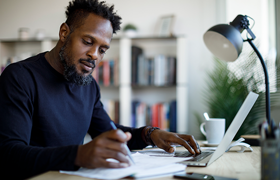 Man working at home in front of computer writing on a piece of paper