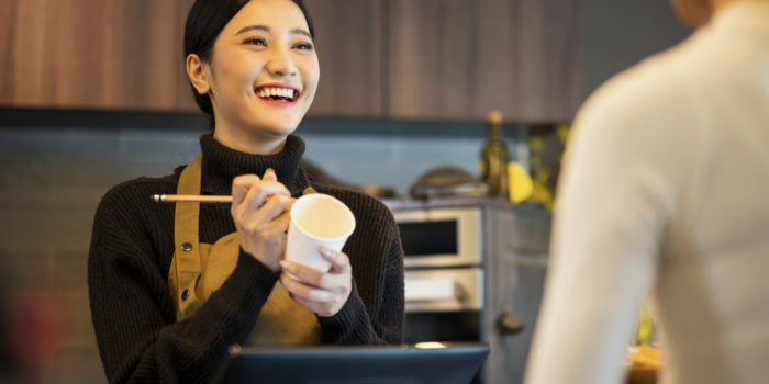 Coffee shop owner taking order and writing customer name on paper cup for ordering. Point of Sale system, Customer Service, and Small Business Solution.