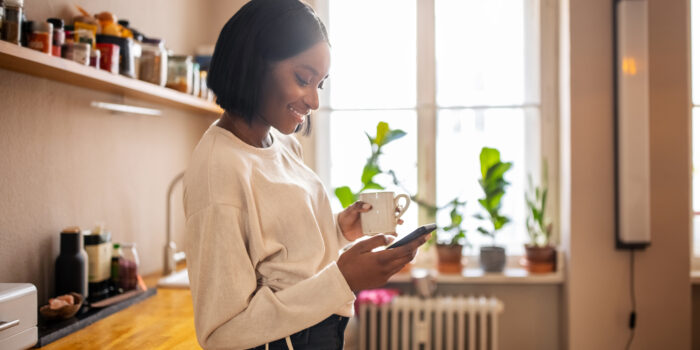 Woman having coffee and texting on her phone at home
