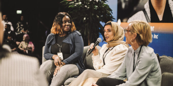 Smiling female entrepreneur looking at colleague interacting with interviewer during panel in convention center