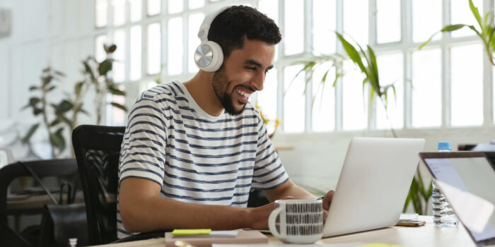 Laughing young man wearing headphones using laptop at desk in office