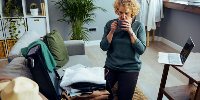 Woman with coffee cup near open travel suitcase