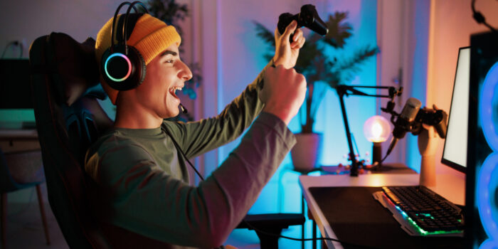 Young teenager plays the computer and celebrates victory in video game with a clenched fist and a smile