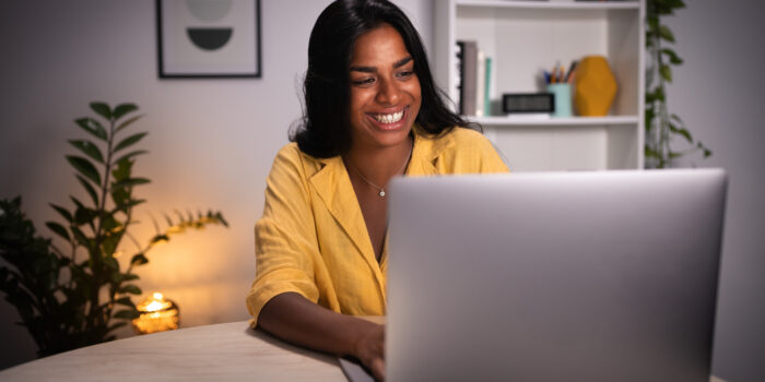 Smiling Indian young woman working late at night with computer at home. Happy female asian college student doing homework using laptop.