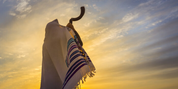 Man in a tallit, Jewish prayer shawl is blowing the shofar ram's horn