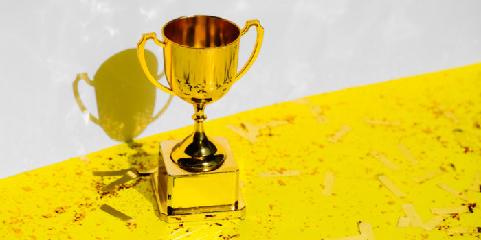 Golden champions cup standing on yellow background with glitter and confetti. Trendy colors of 2021 year