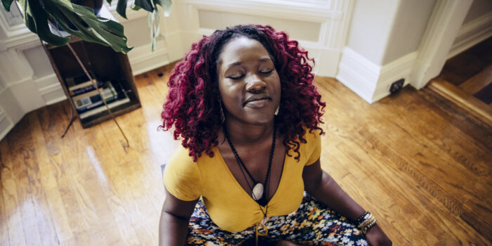 Contented young woman sitting on floor meditating at home