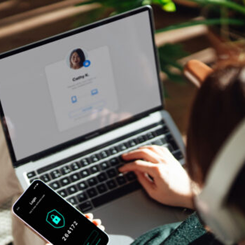Person on their laptop with smartphone in hand opened to a security multi factor authentication app