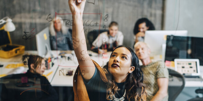 Businesswoman explaining strategy to colleagues while writing on glass at IT company