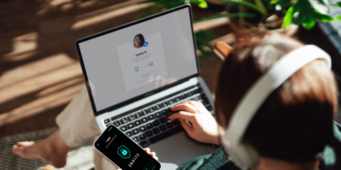 Person on their laptop with a smartphone in one hand displaying a passcode on screen to complete multi-factor authentication