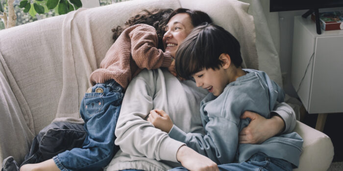 Playful boy and girl with mother on sofa at home