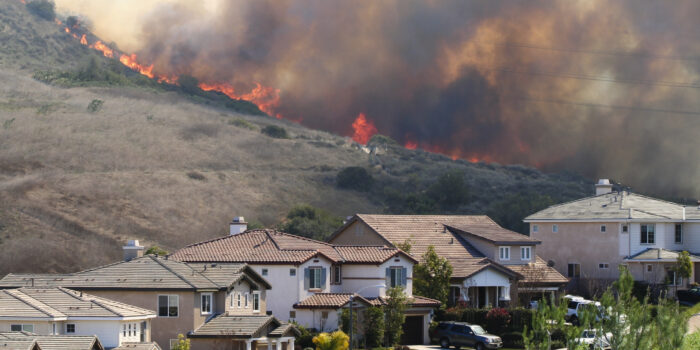 Houses in southern California seen in the foreground while fires are burning nearby on the hills in the background