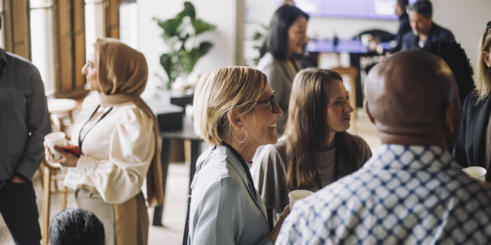 Smiling mature businesswoman having coffee with colleagues in break at convention center