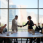 Businesspeople sitting around a conference table and at the head of the table is a man and woman shaking hands