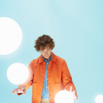 The cover of Weichert's Designing Mobility for Success Research: Part 1 shows a you man in an orange jacket and blue striped dress shirt standing at a white table holding a white orb in his left hand while three other orbs float around him.